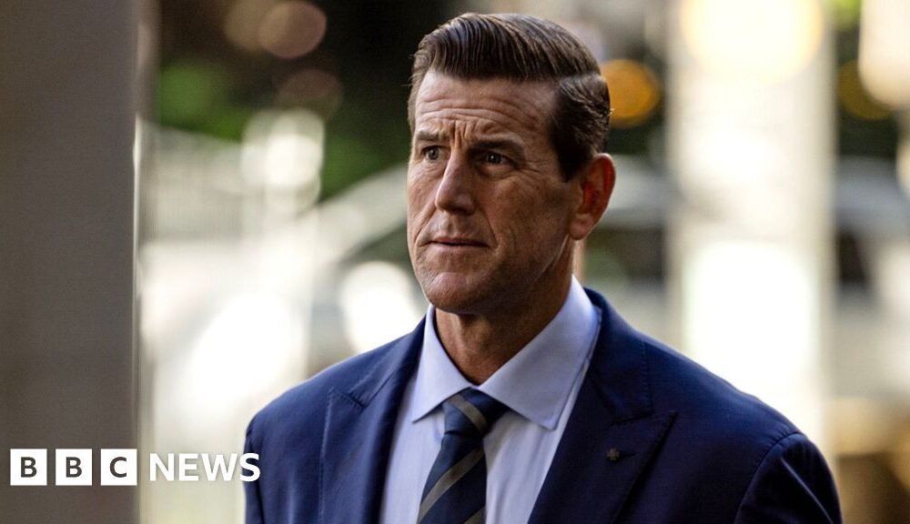 Una fotografía frontal de Roberts-Smith mirando reflexivamente hacia un lado mientras porta corbata y traje, con un fondo borroso, caminando por una calle al llegar a la Corte Federal de Sydney en mayo de 2025.