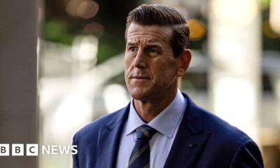 Una fotografía frontal de Roberts-Smith mirando reflexivamente hacia un lado mientras porta corbata y traje, con un fondo borroso, caminando por una calle al llegar a la Corte Federal de Sydney en mayo de 2025.