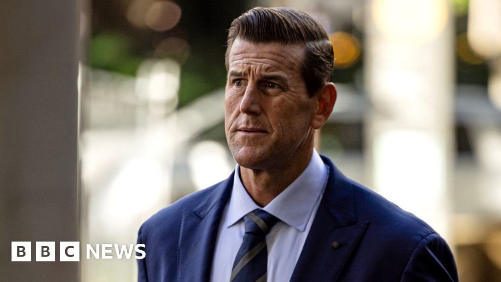 Una fotografía frontal de Roberts-Smith mirando reflexivamente hacia un lado mientras porta corbata y traje, con un fondo borroso, caminando por una calle al llegar a la Corte Federal de Sydney en mayo de 2025.
