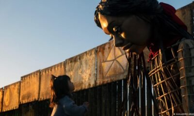 Una niña se acerca a la Pequeña Amal, una marioneta de casi cuatro metros de altura que representa a una niña refugiada siria de diez años, cerca del muro fronterizo entre Estados Unidos y México, en Tijuana. Imagen: GUILLERMO ARIAS/AFP