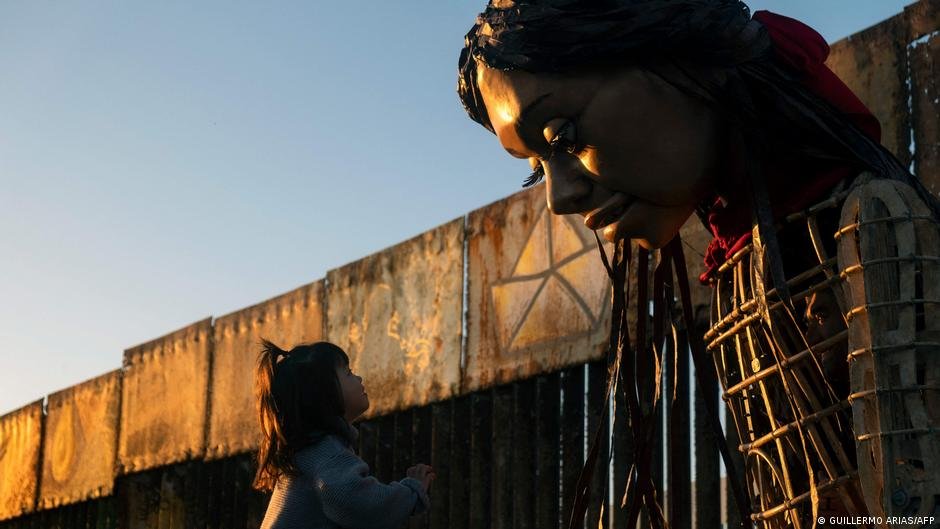 Una niña se acerca a la Pequeña Amal, una marioneta de casi cuatro metros de altura que representa a una niña refugiada siria de diez años, cerca del muro fronterizo entre Estados Unidos y México, en Tijuana. Imagen: GUILLERMO ARIAS/AFP