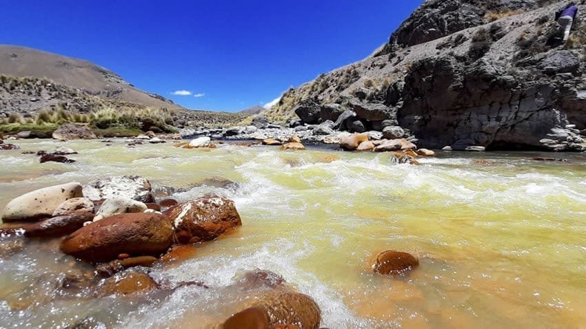 Alcaldes afectados contaminación — Un río de aguas turbias fluye sobre rocas en un paisaje montañoso bajo un cielo azul despejado. Foto de: El Búho