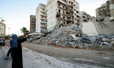 Israel bombardea suburbio — Una mujer toma una foto junto a edificios dañados en el sitio de un bombardeo aéreo israelí que afectó una sucursal en los suburbios sureños de Beirut [Foto: Ibrahim Amro/AFP]