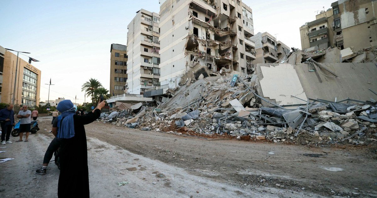 Israel bombardea suburbio — Una mujer toma una foto junto a edificios dañados en el sitio de un bombardeo aéreo israelí que afectó una sucursal en los suburbios sureños de Beirut [Foto: Ibrahim Amro/AFP]