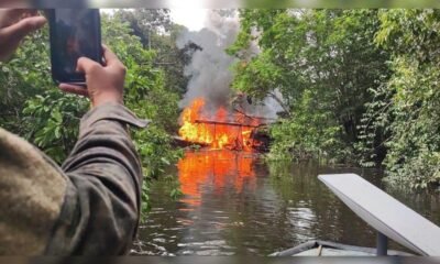 minería ilegal — Una persona toma una fotografía de un gran incendio que arde en la vegetación ribereña de un río. Foto de: La República