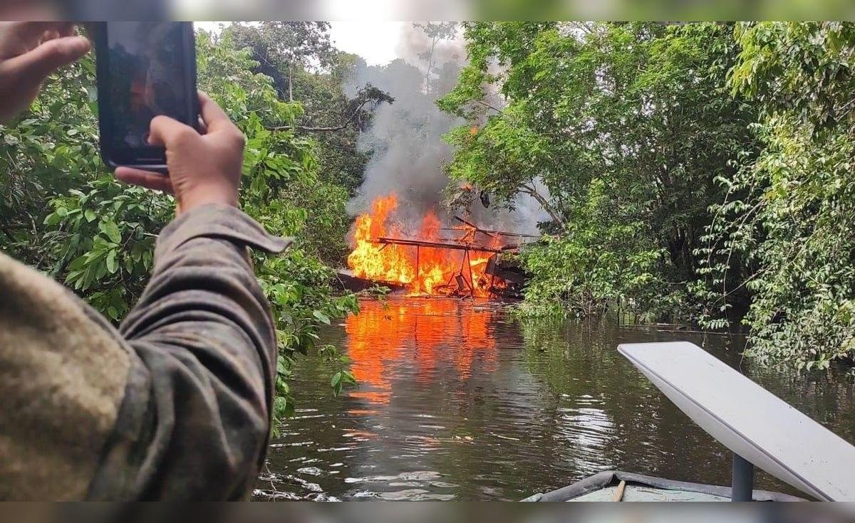 minería ilegal — Una persona toma una fotografía de un gran incendio que arde en la vegetación ribereña de un río. Foto de: La República