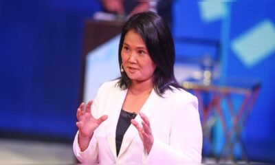 Poder Judicial — Una mujer con blazer blanco y cabello oscuro gesticula mientras habla en un evento con fondo azul. Foto de: La República
