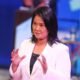 Poder Judicial — Una mujer con blazer blanco y cabello oscuro gesticula mientras habla en un evento con fondo azul. Foto de: La República