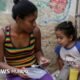 producción mundial — Una mujer alimenta a una niña en el barrio La Bombilla en Caracas.