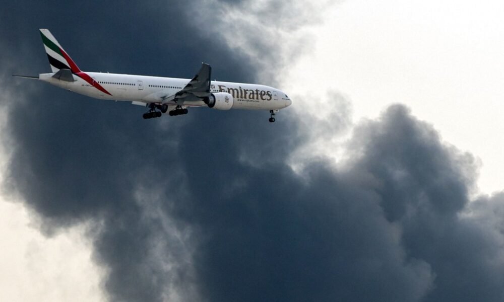 tráfico aéreo — Un avión Boeing 777 de Emirates se prepara para aterrizar mientras una columna de humo emerge de un incendio en el aeropuerto internacional de Dubái en Dubái el 16 de marzo de 2026 [AFP]