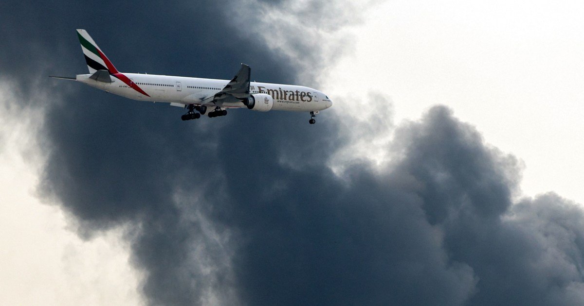 tráfico aéreo — Un avión Boeing 777 de Emirates se prepara para aterrizar mientras una columna de humo emerge de un incendio en el aeropuerto internacional de Dubái en Dubái el 16 de marzo de 2026 [AFP]