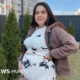 Ucrania debate ley — Una mujer embarazada está de pie en un jardín con la mano sobre el vientre. Tiene el pelo largo, liso y oscuro, y lleva un conjunto de blusa y pantalón blancos con detalles negros. También lleva una sudadera con capucha de color marrón claro.