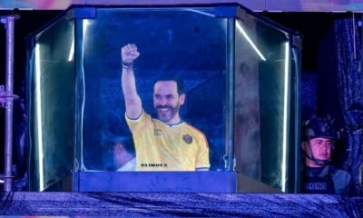 estrecha ventaja — El futbolista Sergio Agüero celebra con el puño en alto mientras aparece dentro de una estructura transparente iluminada. Foto de: news.google.com