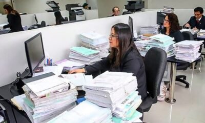 gratificaciones y CTS trabajadores — Mujeres trabajan en oficinas con grandes pilas de papeles y carpetas sobre los escritorios frente a monitores. Foto de: Gestión