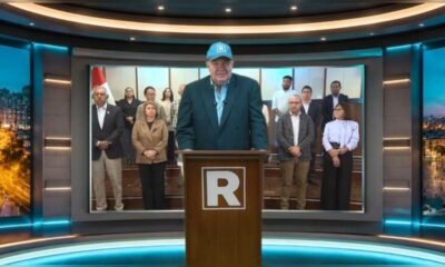 López Aliaga — Un hombre con una gorra azul y chaqueta oscura habla ante un podio en un estudio de televisión con personas al fondo. Foto de: La República