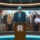 López Aliaga — Un hombre con una gorra azul y chaqueta oscura habla ante un podio en un estudio de televisión con personas al fondo. Foto de: La República