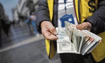 Dólar estadounidense — Unas manos sostienen fajos de dólares estadounidenses en un entorno urbano, ilustrando la fluctuación del tipo de cambio. Foto de: Gestión