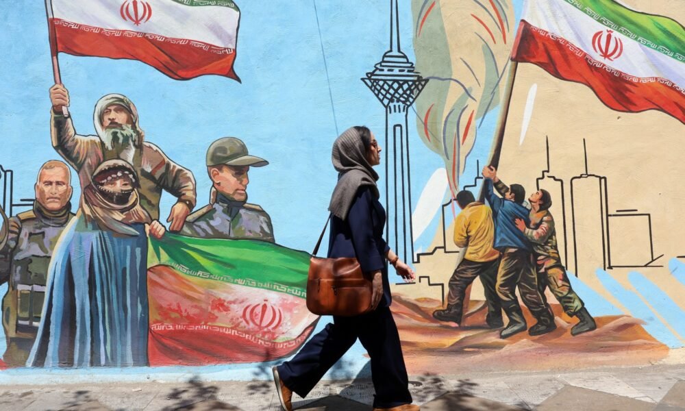 Irán avanza negociaciones — Una mujer iraní camina por una calle de Teherán pasando junto a un mural colorido pintado en la pared. Foto de: EPA