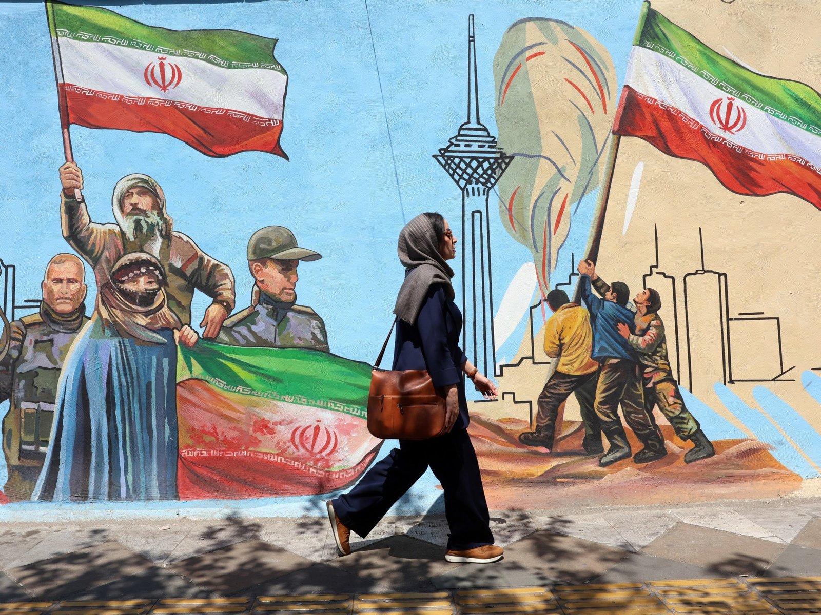 Irán avanza negociaciones — Una mujer iraní camina por una calle de Teherán pasando junto a un mural colorido pintado en la pared. Foto de: EPA
