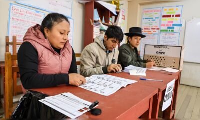 segunda vuelta — Tres personas están sentadas en una mesa roja, revisando documentos y materiales de trabajo. Foto de: La República