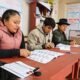 segunda vuelta — Tres personas están sentadas en una mesa roja, revisando documentos y materiales de trabajo. Foto de: La República