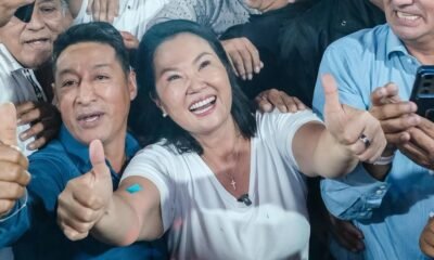 fraude electoral — Una mujer sonriente y un hombre a su lado muestran el pulgar hacia arriba frente a otras personas. Foto de: El Búho
