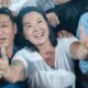fraude electoral — Una mujer sonriente y un hombre a su lado muestran el pulgar hacia arriba frente a otras personas. Foto de: El Búho