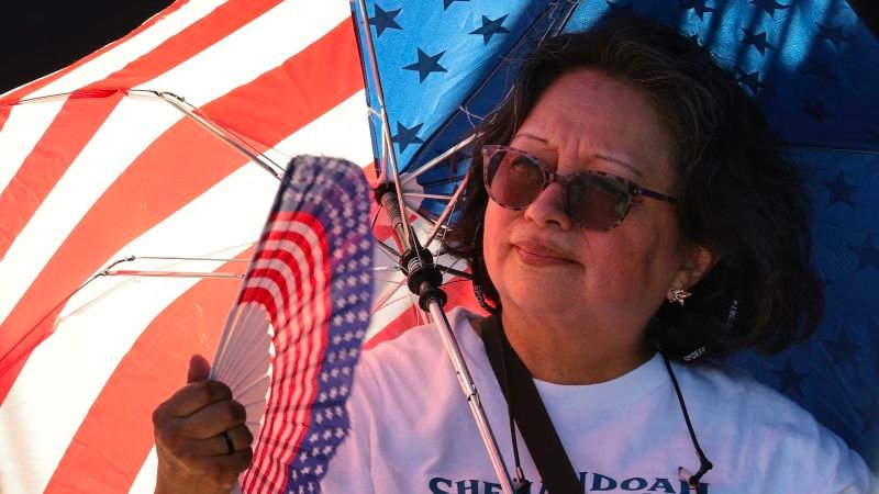 ola de calor — Una mujer sostiene un abanico con motivos de la bandera estadounidense mientras se prepara para las celebraciones del 4 de julio. Foto de: CNN en Español