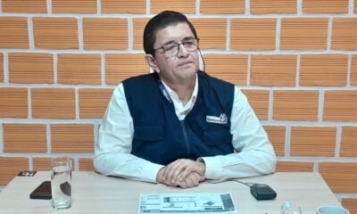 padrón electoral — Un hombre con gafas y chaleco azul sentado ante una mesa con documentos y un vaso de agua frente a una pared de ladrillos. Foto de: El Búho