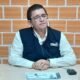 padrón electoral — Un hombre con gafas y chaleco azul sentado ante una mesa con documentos y un vaso de agua frente a una pared de ladrillos. Foto de: El Búho