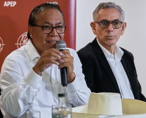 votos extranjeros Perú — Dos hombres con gafas y camisas blancas hablan frente a un micrófono en un evento con el logo de APEP. Foto de: news.google.com