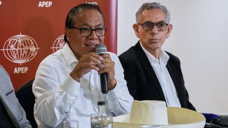 votos extranjeros Perú — Dos hombres con gafas y camisas blancas hablan frente a un micrófono en un evento con el logo de APEP. Foto de: news.google.com