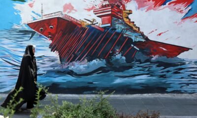 acuerdo Irán — Una persona camina frente a un mural que muestra un barco en llamas, simbolizando la inestabilidad y tensión en el conflicto de Medio Oriente. Foto de: news.google.com