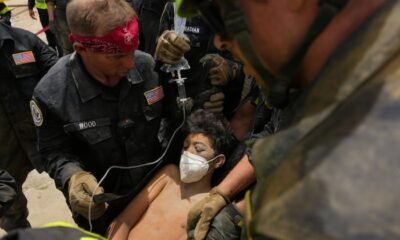Venezuela enfrenta devastación — Un rescatista con pañuelo rojo y uniforme oscuro asiste a una persona que usa mascarilla mientras otros uniformados observan. Foto de: news.google.com