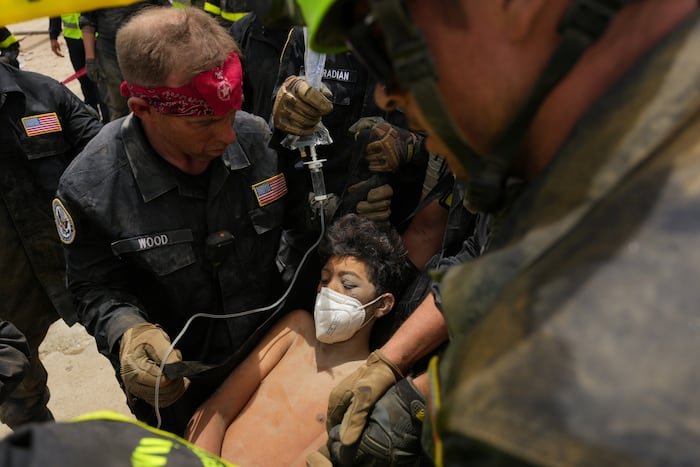 Venezuela enfrenta devastación — Un rescatista con pañuelo rojo y uniforme oscuro asiste a una persona que usa mascarilla mientras otros uniformados observan. Foto de: news.google.com