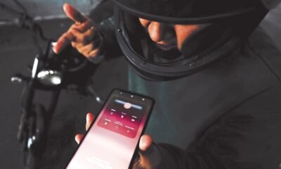 Amenazas través WhatsApp — Una persona sostiene un teléfono móvil mostrando una aplicación de mensajería mientras se encuentra cerca de una motocicleta. Foto de: Gestión