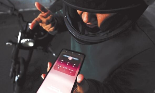 Amenazas través WhatsApp — Una persona sostiene un teléfono móvil mostrando una aplicación de mensajería mientras se encuentra cerca de una motocicleta. Foto de: Gestión