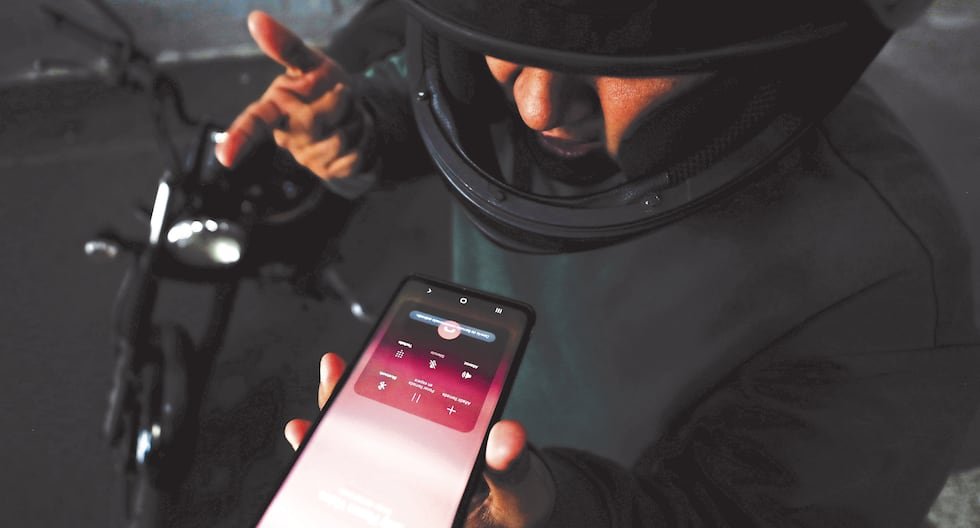 Amenazas través WhatsApp — Una persona sostiene un teléfono móvil mostrando una aplicación de mensajería mientras se encuentra cerca de una motocicleta. Foto de: Gestión