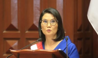 sueldo mínimo — Una mujer con gafas y vestimenta azul habla frente a un podio con micrófonos en un interior de madera. Foto de: Gestión