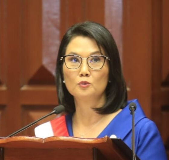 sueldo mínimo — Una mujer con gafas y vestimenta azul habla frente a un podio con micrófonos en un interior de madera. Foto de: Gestión