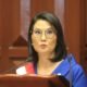 sueldo mínimo — Una mujer con gafas y vestimenta azul habla frente a un podio con micrófonos en un interior de madera. Foto de: Gestión