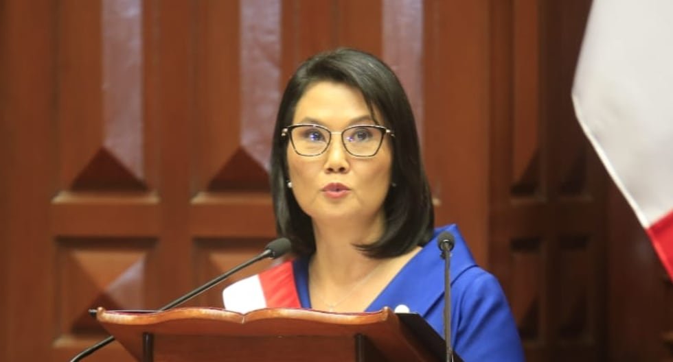 sueldo mínimo — Una mujer con gafas y vestimenta azul habla frente a un podio con micrófonos en un interior de madera. Foto de: Gestión