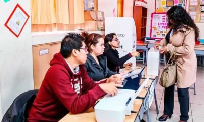 Elecciones Regionales — Dos personas atienden a una mujer en el mostrador de una oficina con equipos electrónicos y carteles informativos. Foto de: El Peruano