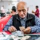 pensión adicional fiestas patrias — Un hombre mayor revisa sus documentos y dinero en una ventanilla de atención, representando a los pensionistas que recibirán un pago adicional. Foto de: El Peruano