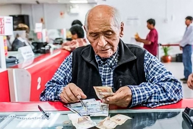 pensión adicional fiestas patrias — Un hombre mayor revisa sus documentos y dinero en una ventanilla de atención, representando a los pensionistas que recibirán un pago adicional. Foto de: El Peruano