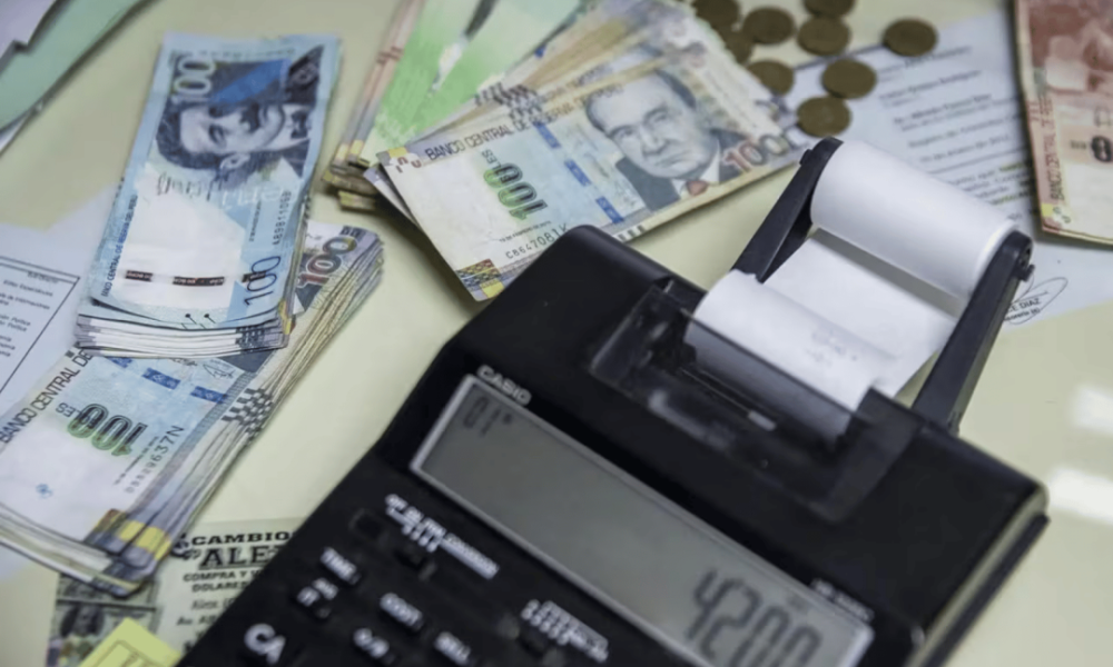 Peruanos usarán — Una calculadora con un rollo de papel muestra el número 4200 junto a billetes de cien pesos argentinos y monedas doradas. Foto de: Perú21