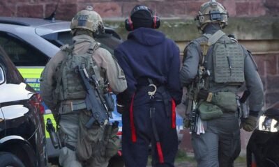 ataque nord stream Ucrania — Dos agentes con equipo táctico y cascos protegen a una persona con capucha en medio de una calle. Foto de: Al Jazeera
