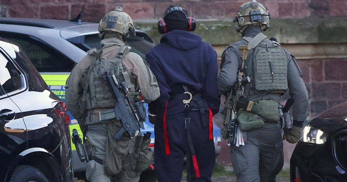 ataque nord stream Ucrania — Dos agentes con equipo táctico y cascos protegen a una persona con capucha en medio de una calle. Foto de: Al Jazeera