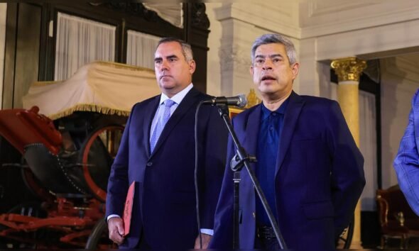 Catherin Palomino — Pedro Sánchez y Fernando Grande-Marlaska aparecen en un escenario con un micrófono y un fondo decorado con cortinajes. Foto de: La República