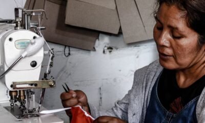 Lima Metropolitana — Una mujer de rasgos asiáticos opera una máquina de coser industrial mientras sostiene una pieza de tela roja. Foto de: Gestión